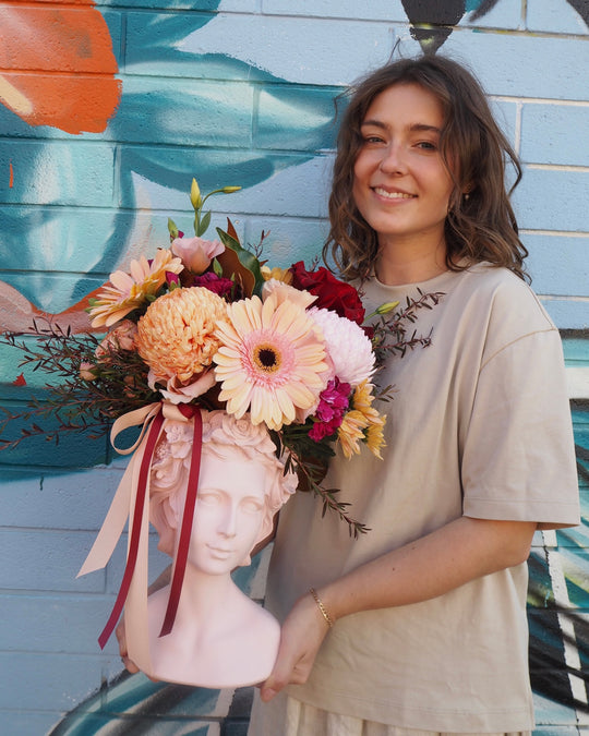 Woman holding a bouquet of flowers in front of a colorful mural.