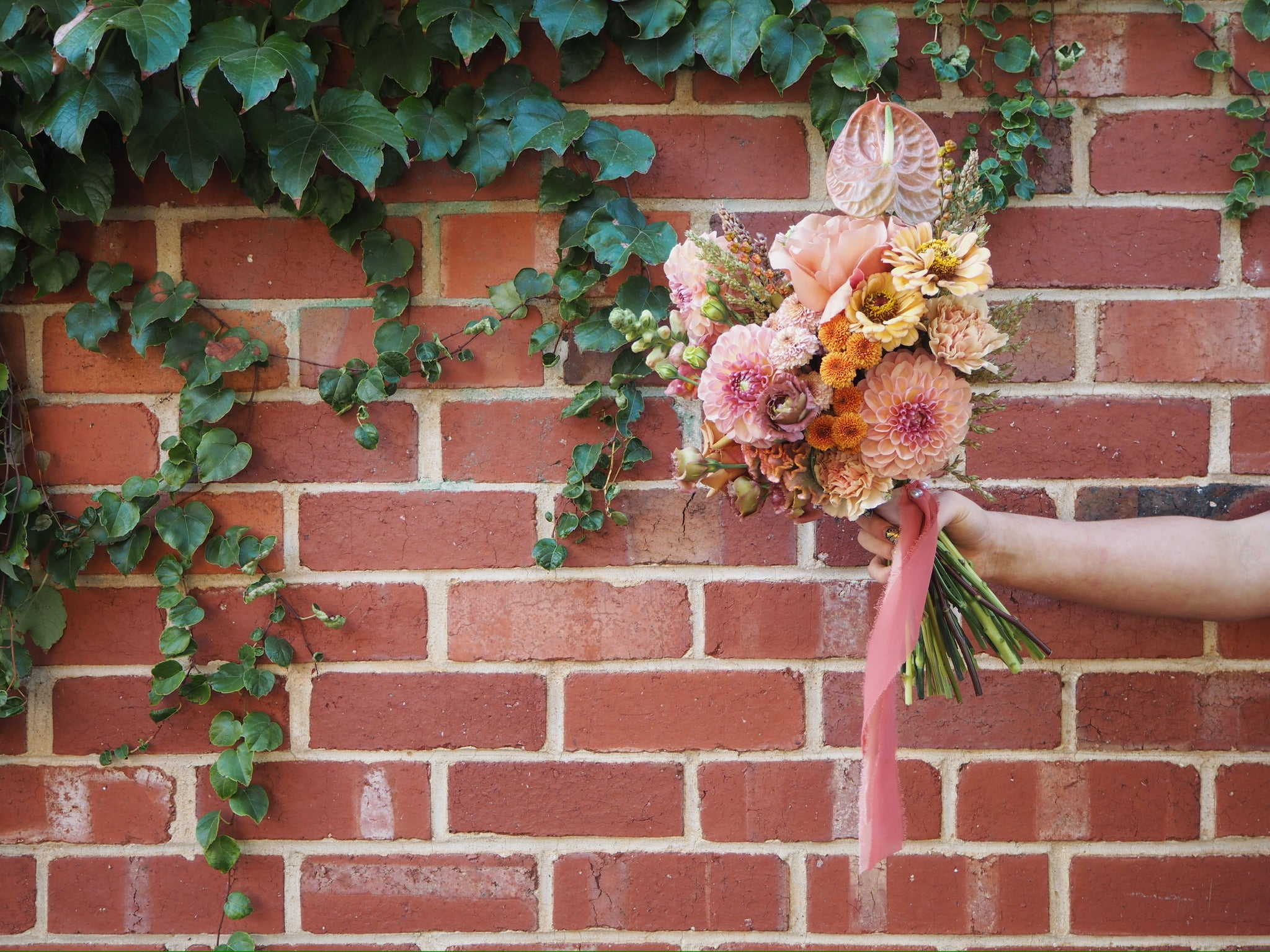 Bridal bouquet of flowers held against a brick wall with greenery