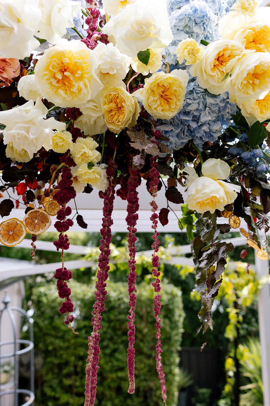 Decorative floral arrangement with white, yellow, and blue flowers, and hanging pink amaranthus