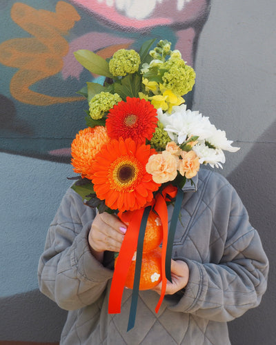 Person holding a bouquet of flowers in front of their face against a colorful wall.