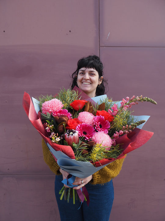Person holding a large bouquet of flowers in front of a purple wall