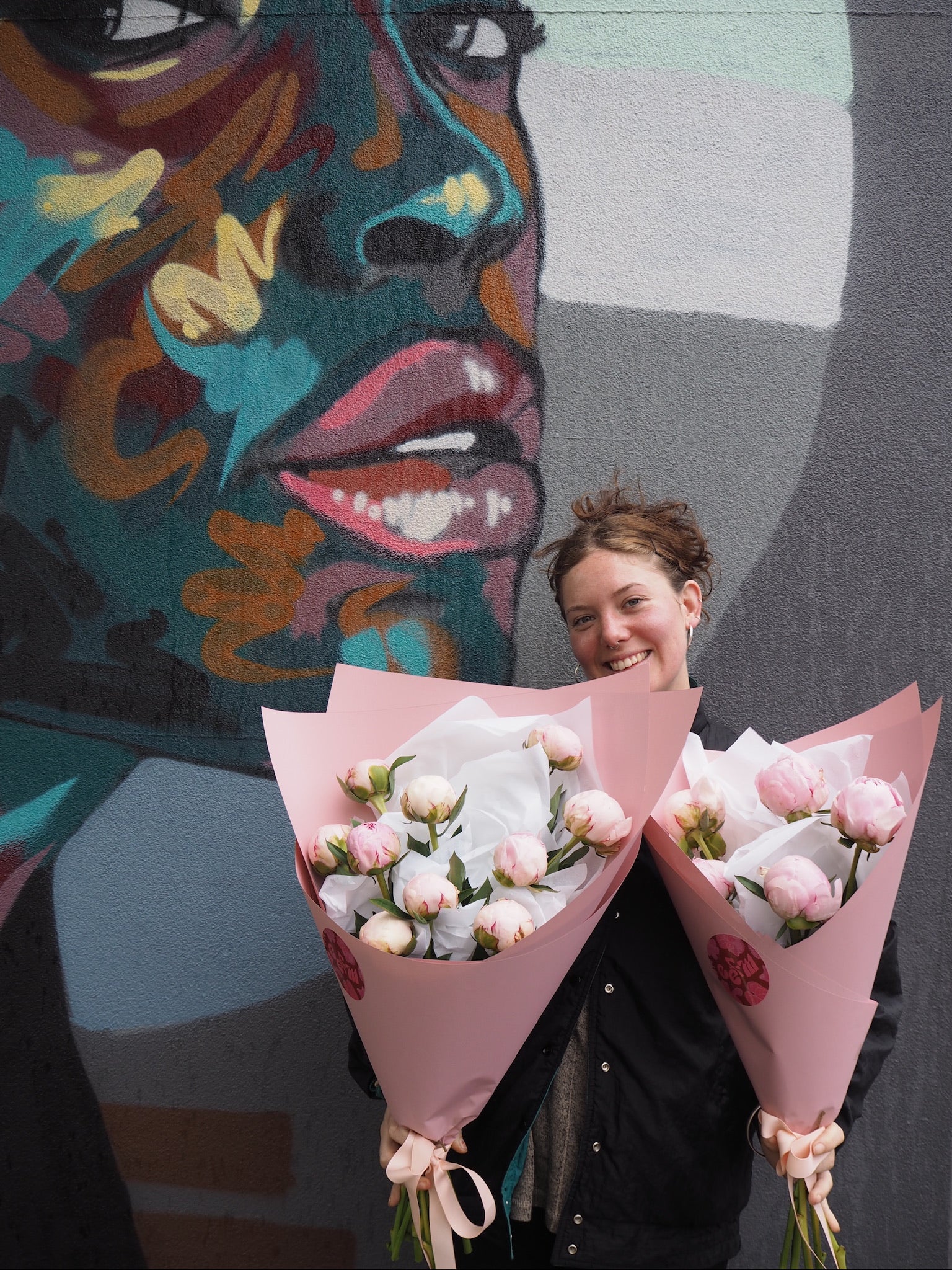 Woman holding a bouquet of flowers in front of a colorful mural.
