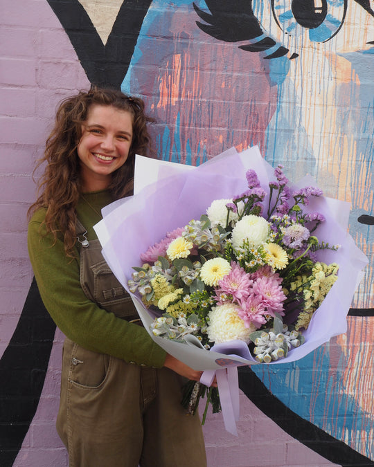 Person holding a bouquet of flowers in front of a colorful mural.