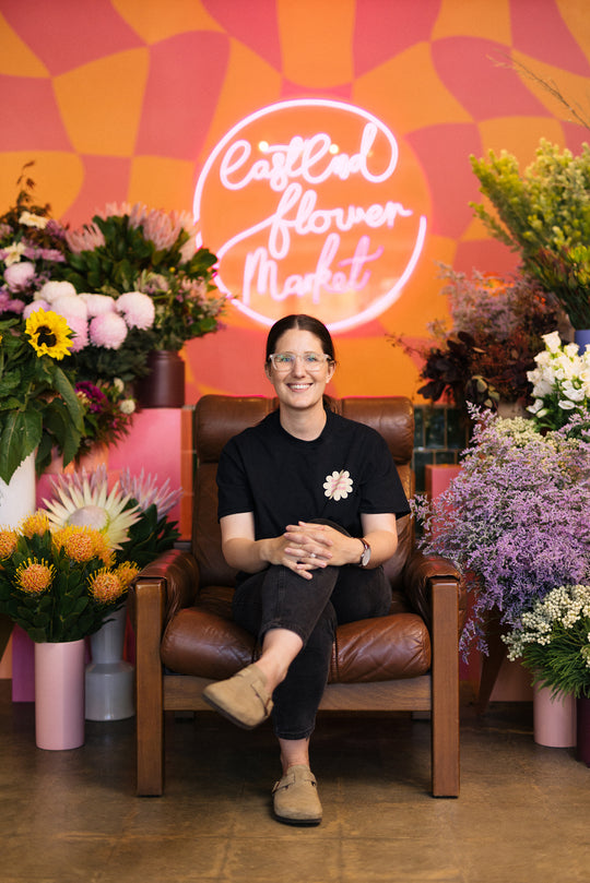 Woman sitting in a chair surrounded by flowers with a colorful wall in the background
