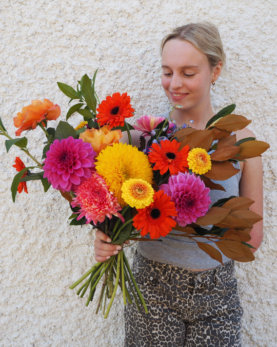 Woman holding a vibrant bouquet of flowers against a textured wall.
