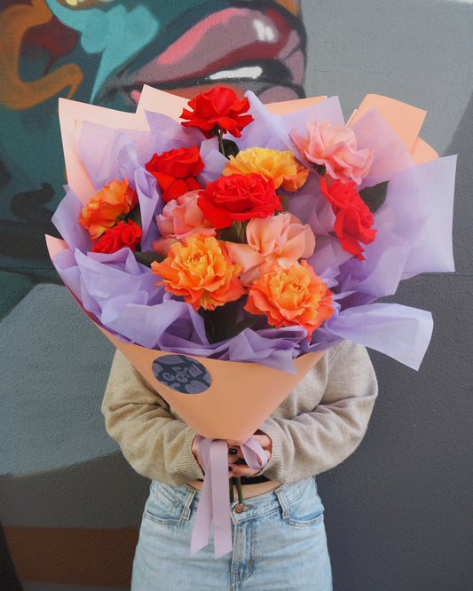 Person holding a bouquet of colourful roses against a dark background
