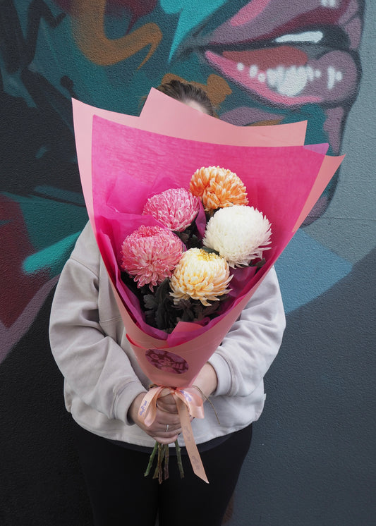 Person holding a bouquet of flowers wrapped in pink paper against a colorful background
