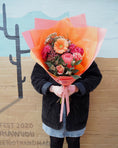 Load image into Gallery viewer, Person holding a bouquet of flowers against a wall with cactus designs and text.
