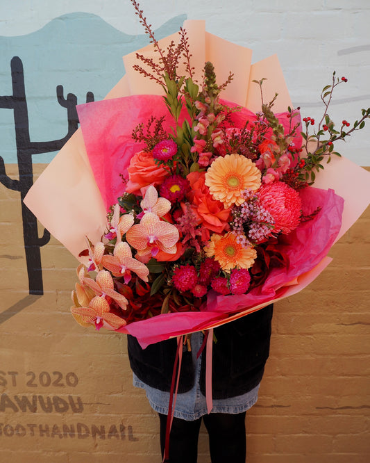 Bouquet of flowers with pink and orange tones held by a person against a painted wall mural.