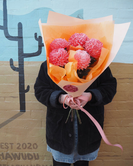 Person holding a wrapped bouquet of 5 stems of coral chrysanthemums. 