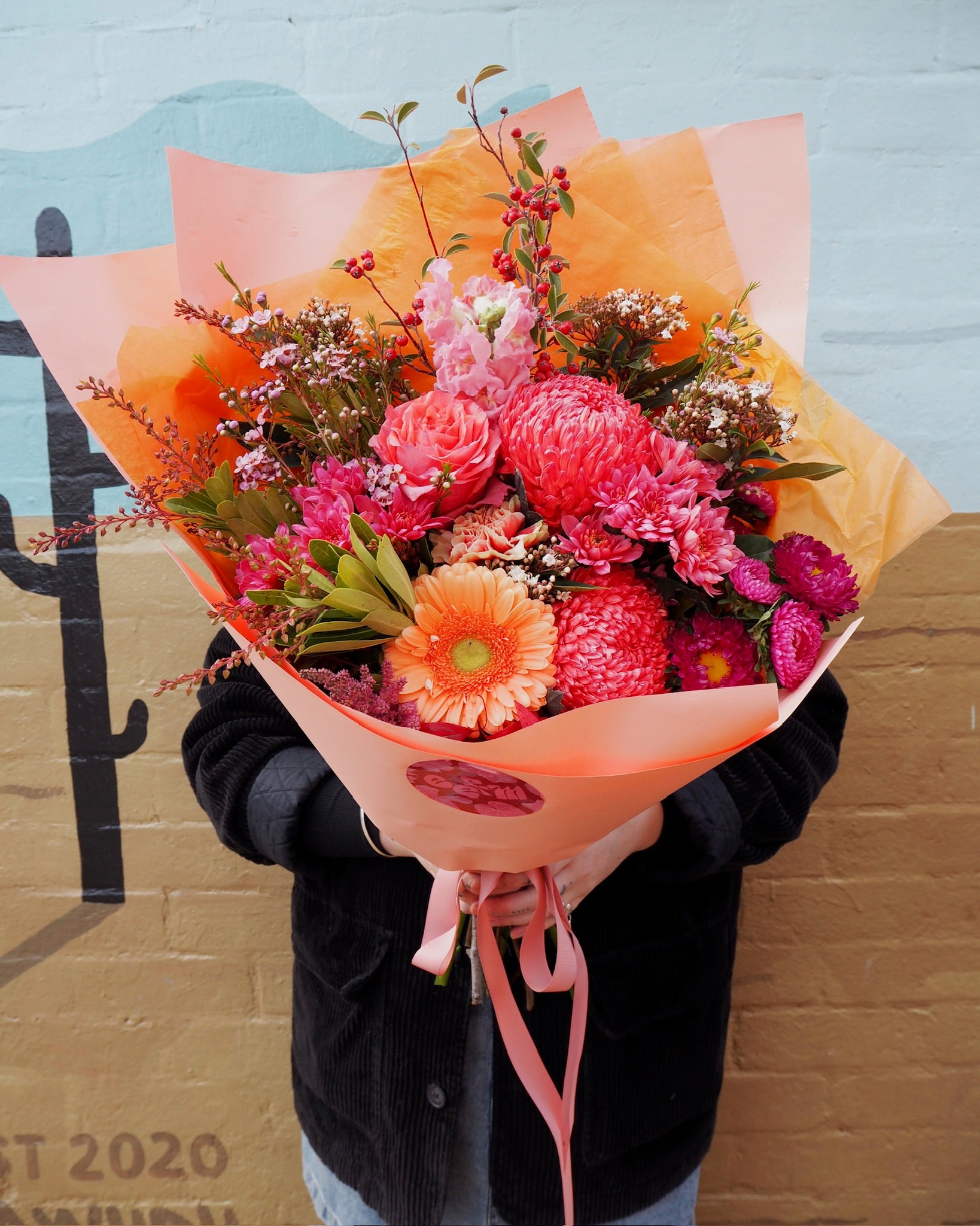 Bouquet of flowers held by a person in front of a colorful wall.