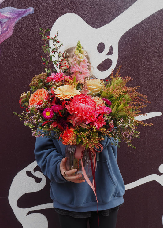 Person holding a vibrant bouquet of flowers against a dark background with abstract designs.