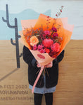Load image into Gallery viewer, Person holding a bouquet of coral and hot pink flowers in front of a mural with cacti.
