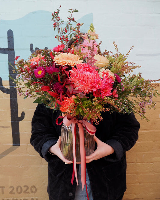 Person holding a vibrant bouquet of flowers against a colorful wall.