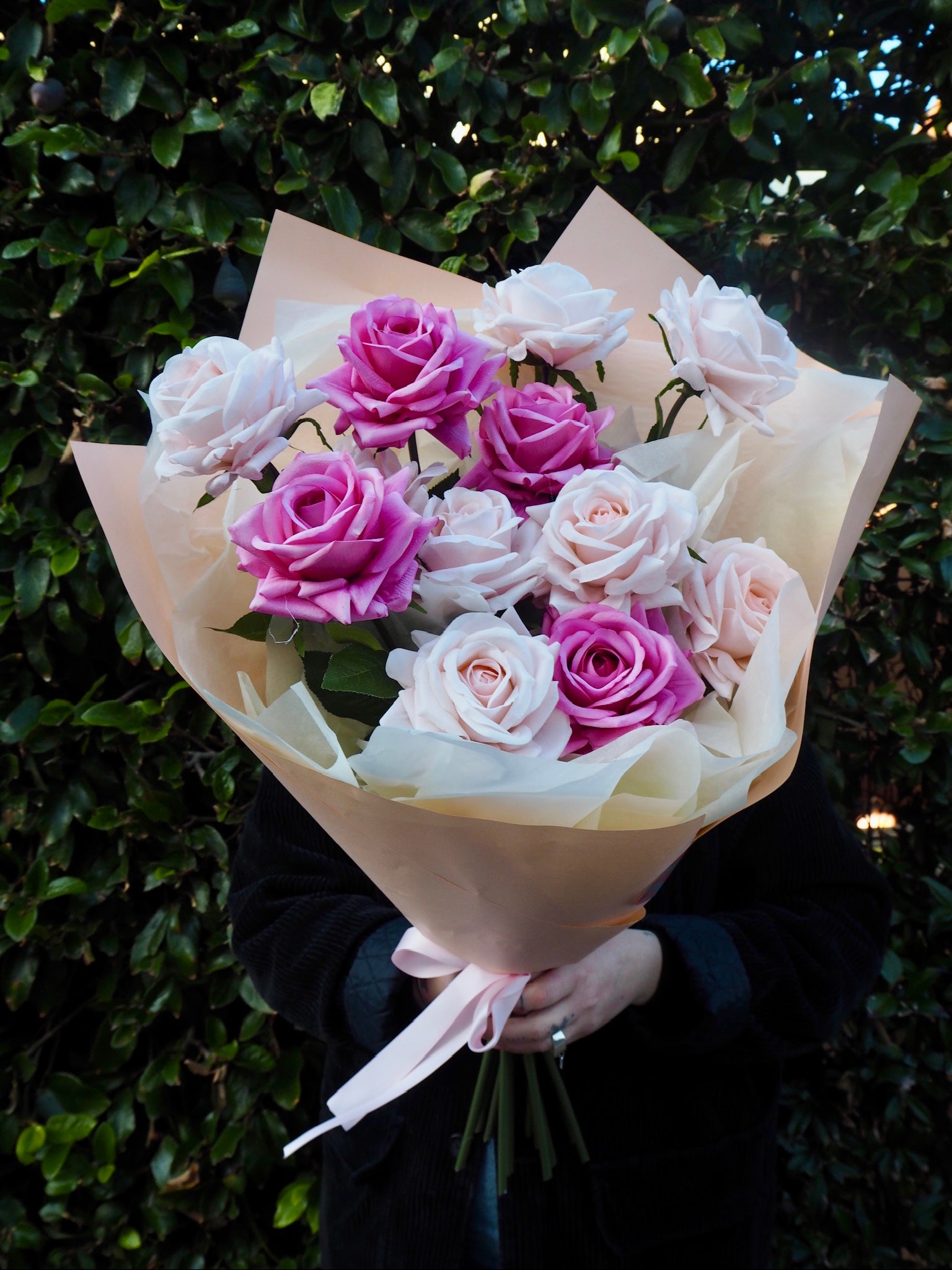 Person holding a bouquet of one dozen faux, real-touch roses in shades of pink.