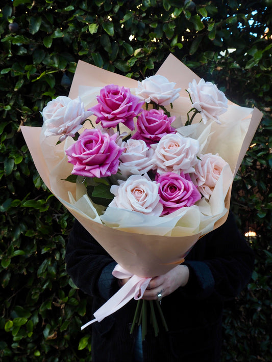 Person holding a bouquet of one dozen faux, real-touch roses in shades of pink.