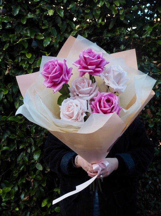 Person holding a bouquet of 6 faux, real-touch roses in shades of pink. 