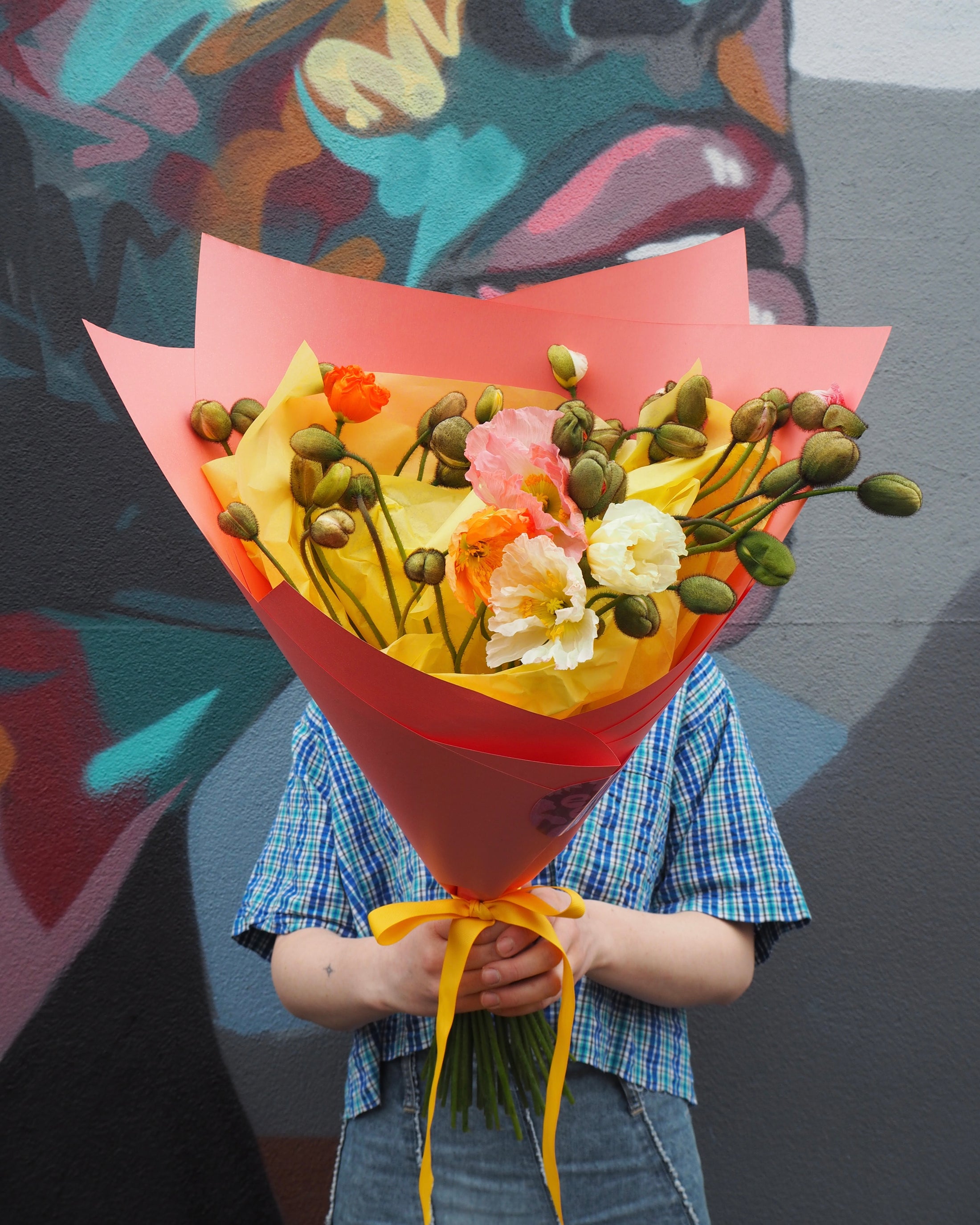 Person holding a bouquet of poppies in front of a colourful mural.