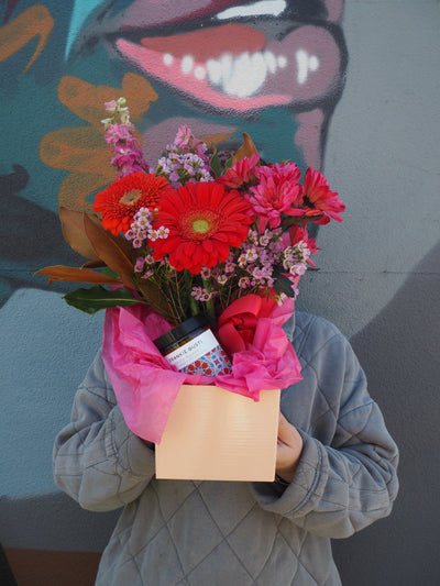 Person holding a bouquet of flowers with a card against a colorful wall.