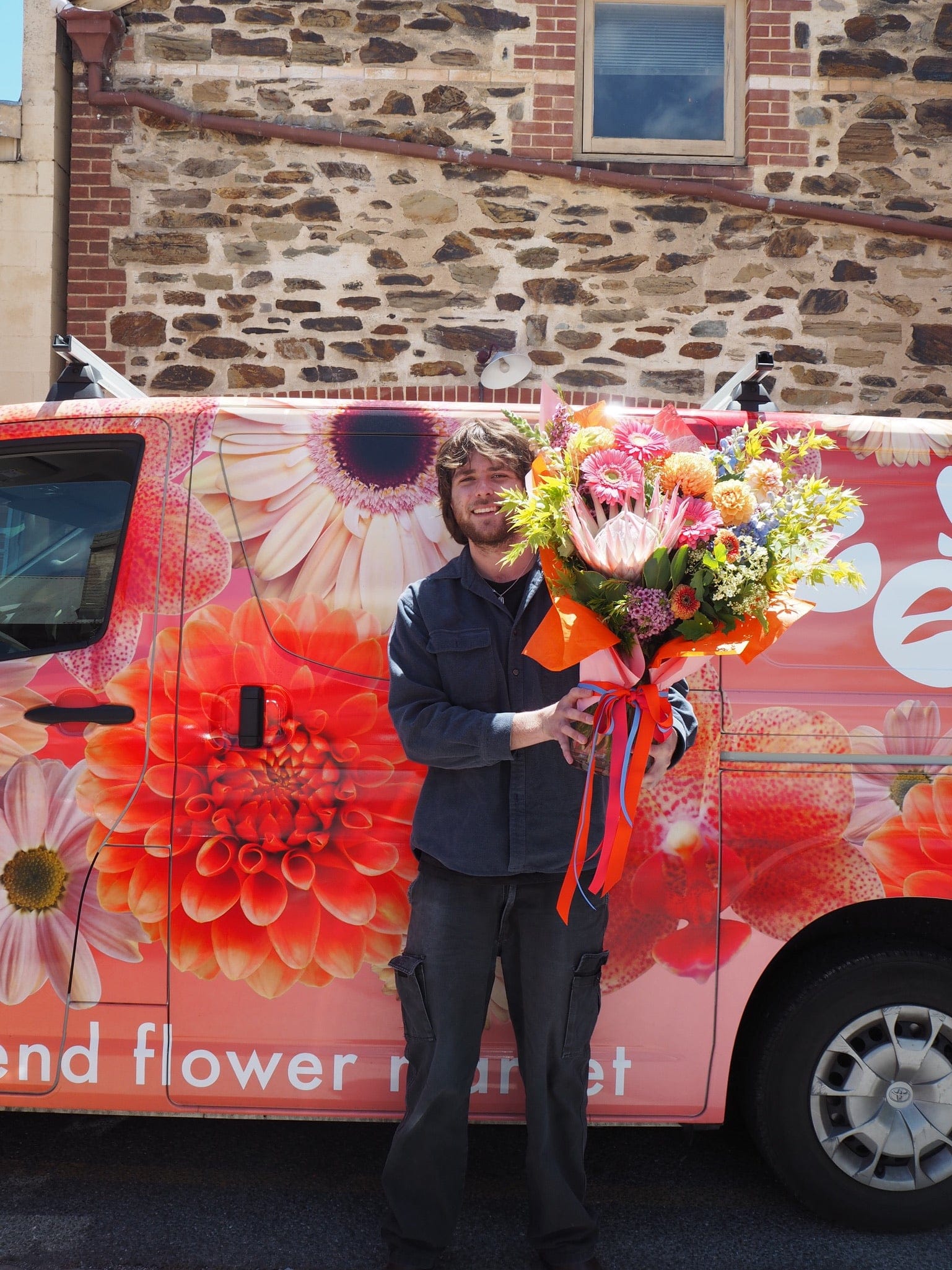 Person holding a bouquet of flowers in front of a floral-themed van.