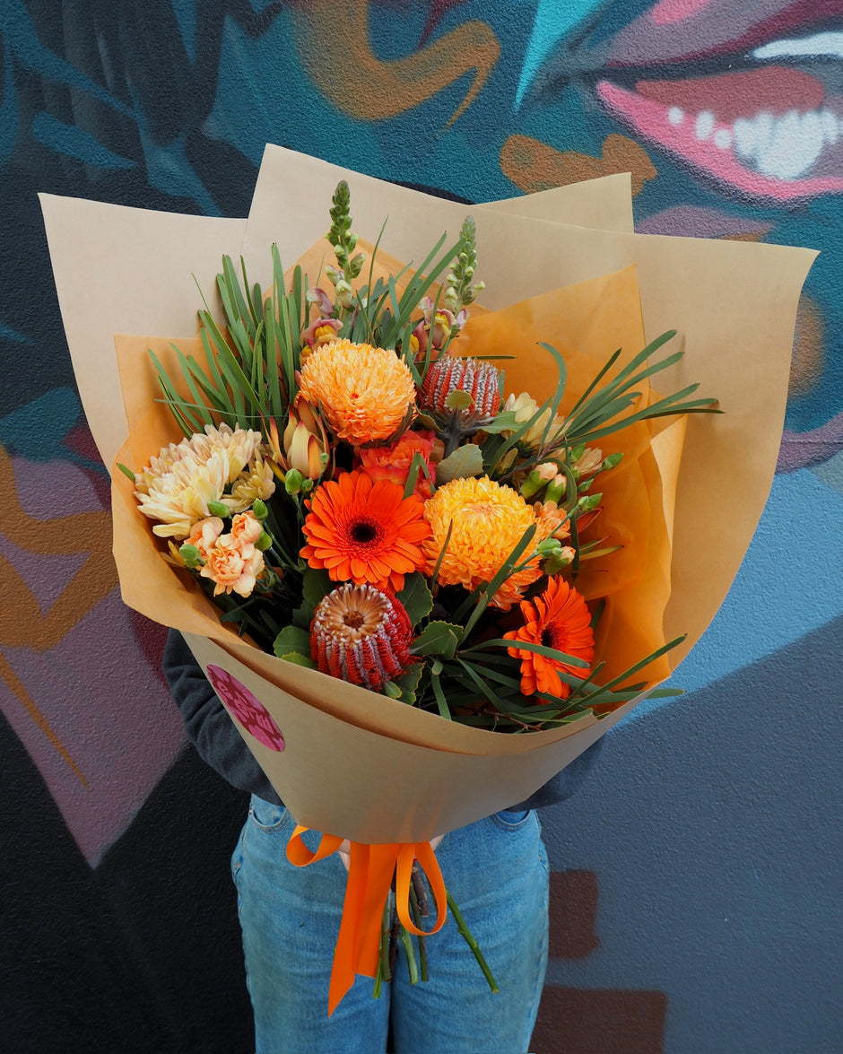 Bouquet of flowers with orange and yellow colors held by a person against a colorful abstract background.
