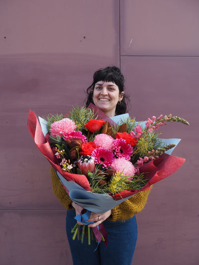 Person holding a large bouquet of flowers in front of a purple wall