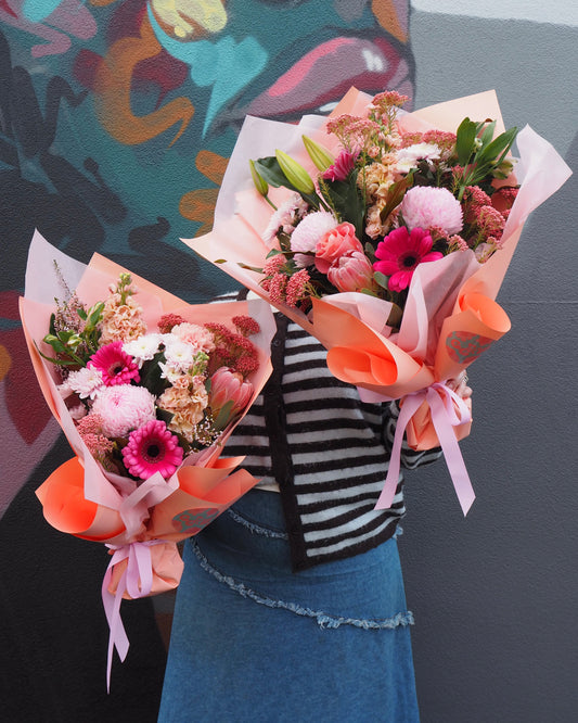 person holding two pink bouquets against a grey wall