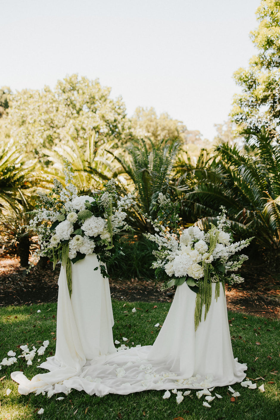 Two white floral arrangements on a grassy outdoor setting.