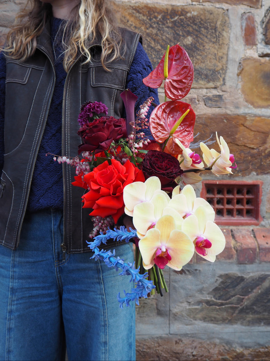 Person holding a colorful bouquet of flowers against a stone wall.