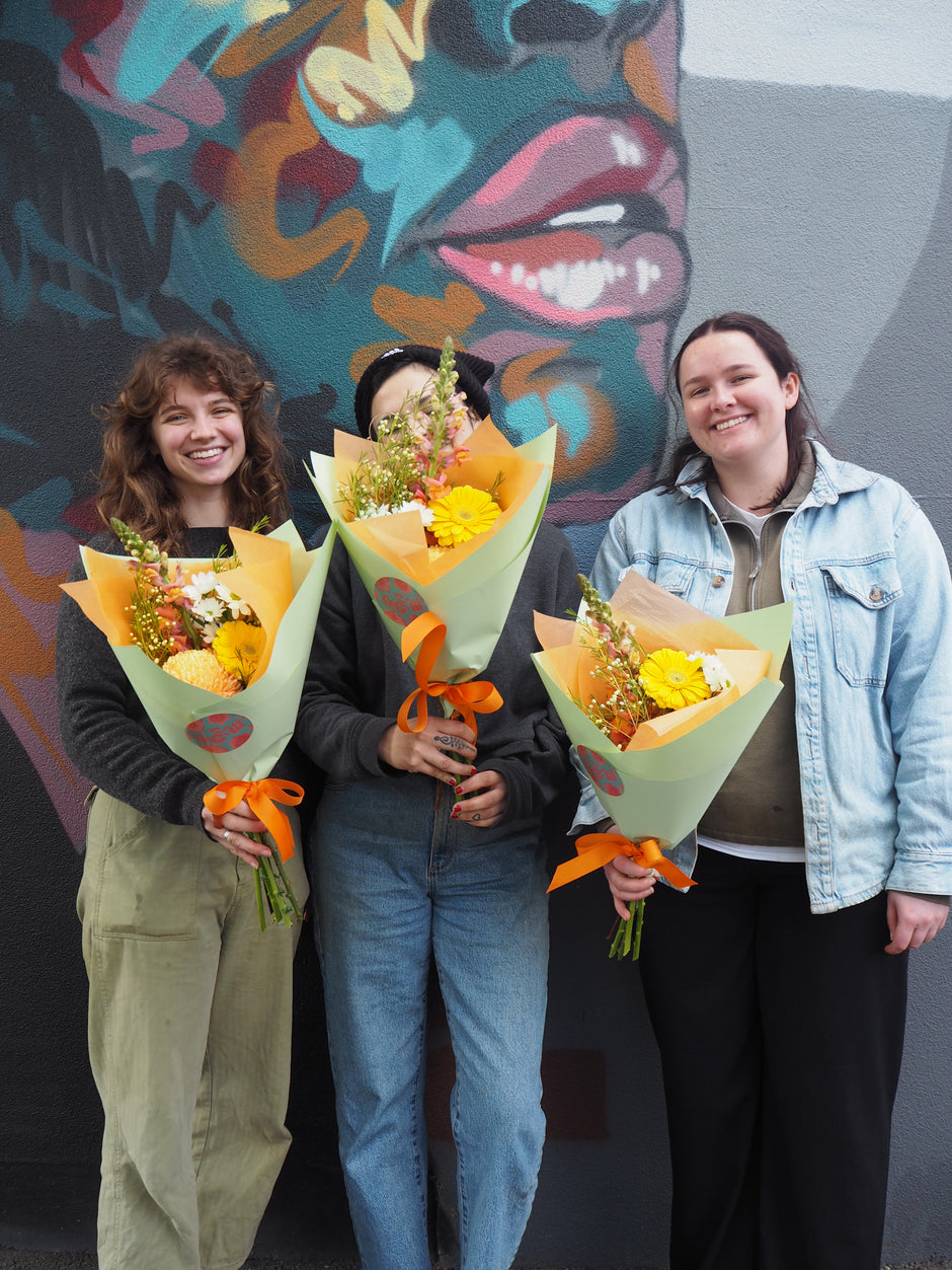 Three people holding flower bouquets on a colourful floor.