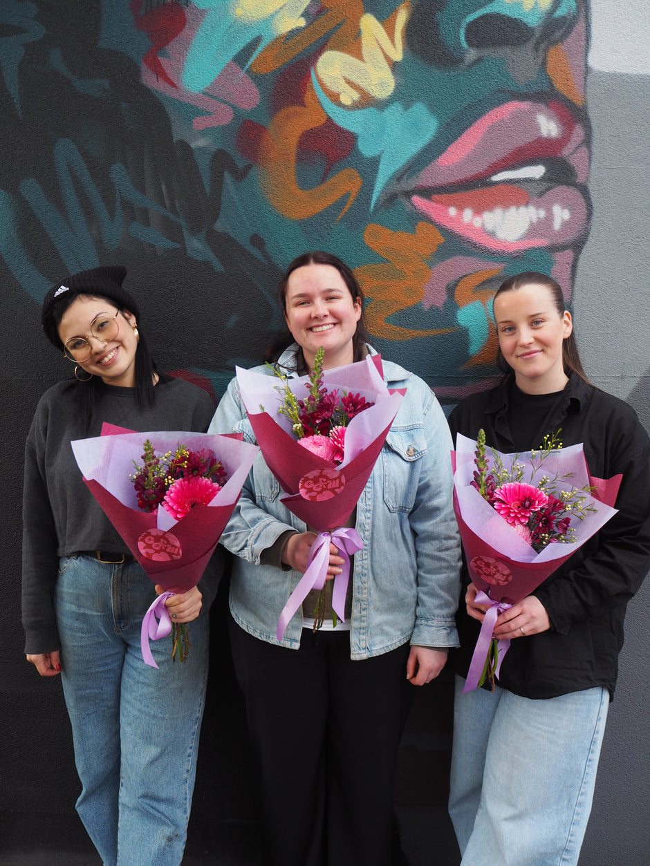 Three people holding flowers against a colourful mural.