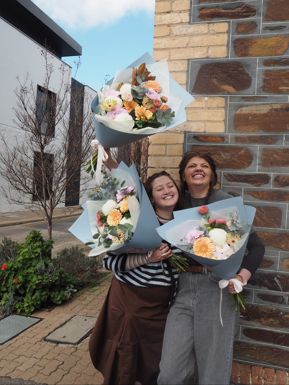 Two women holding bouquets of flowers in front of a brick building.
