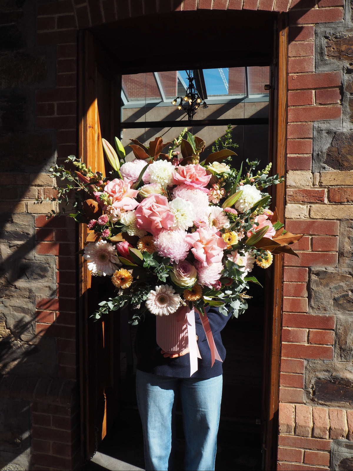Person holding a large bouquet of flowers in front of a brick wall.