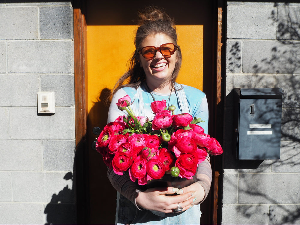 Woman holding pink flowers in front of a yellow door.