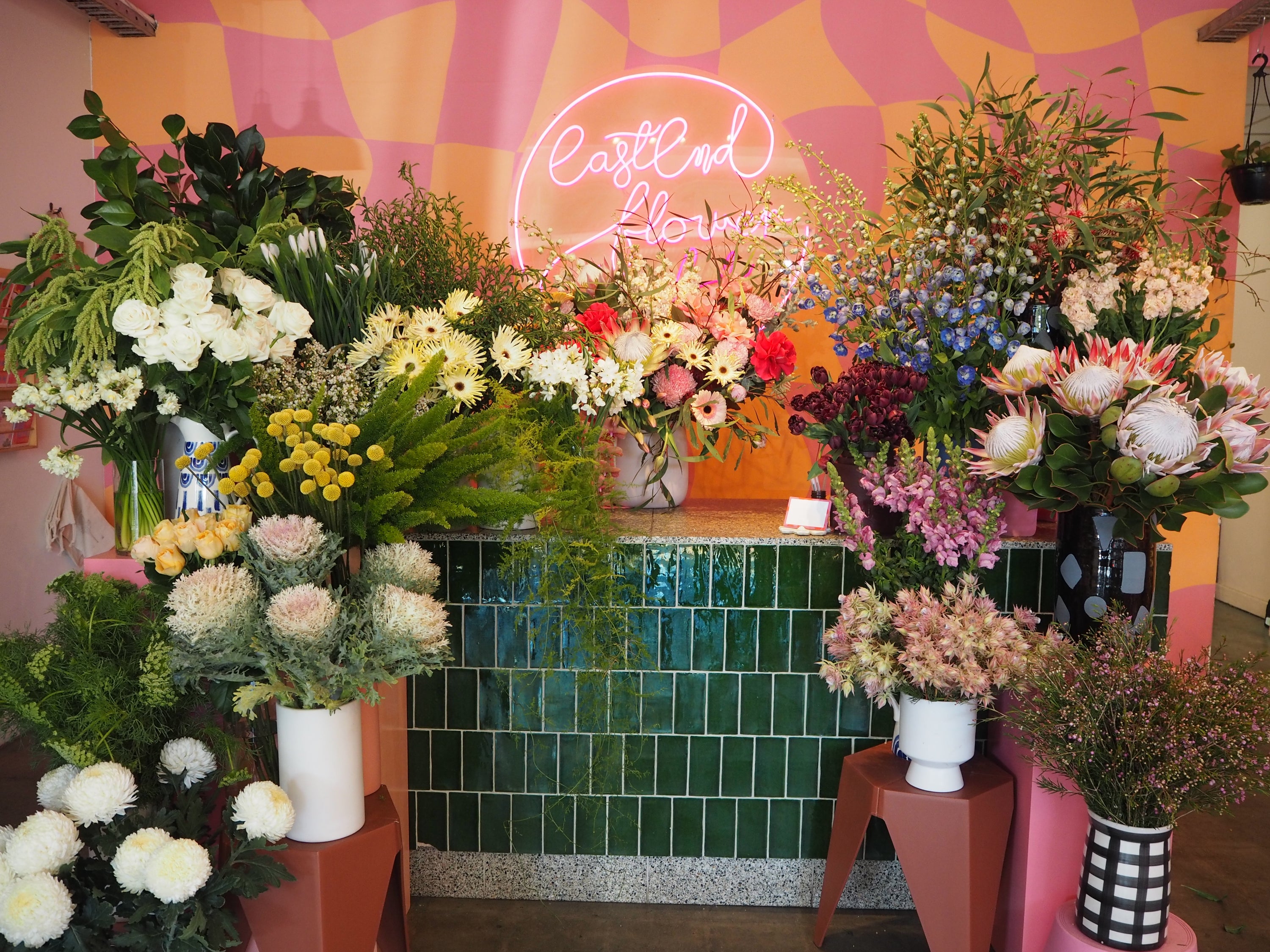 Floral arrangements in front of a colorful wall with a neon sign.