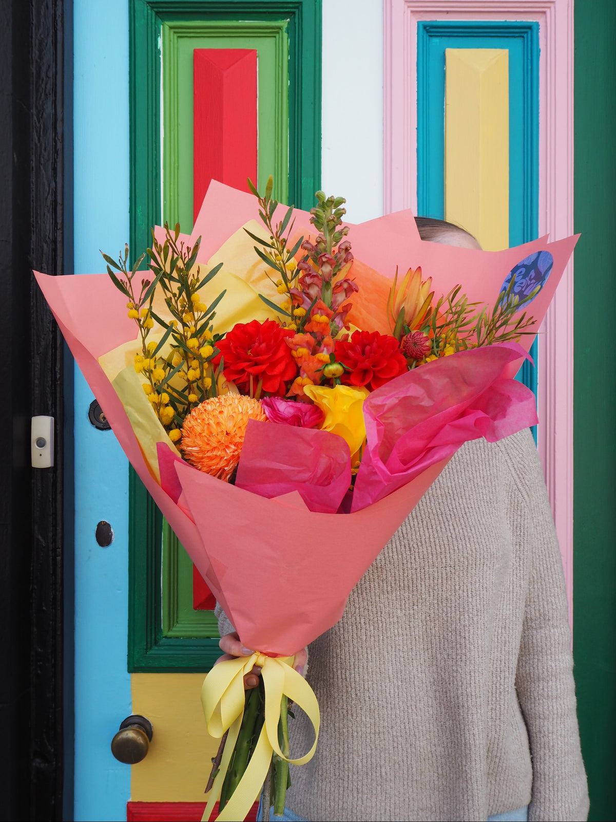Person holding a colorful bouquet of flowers in front of a multicolored door.